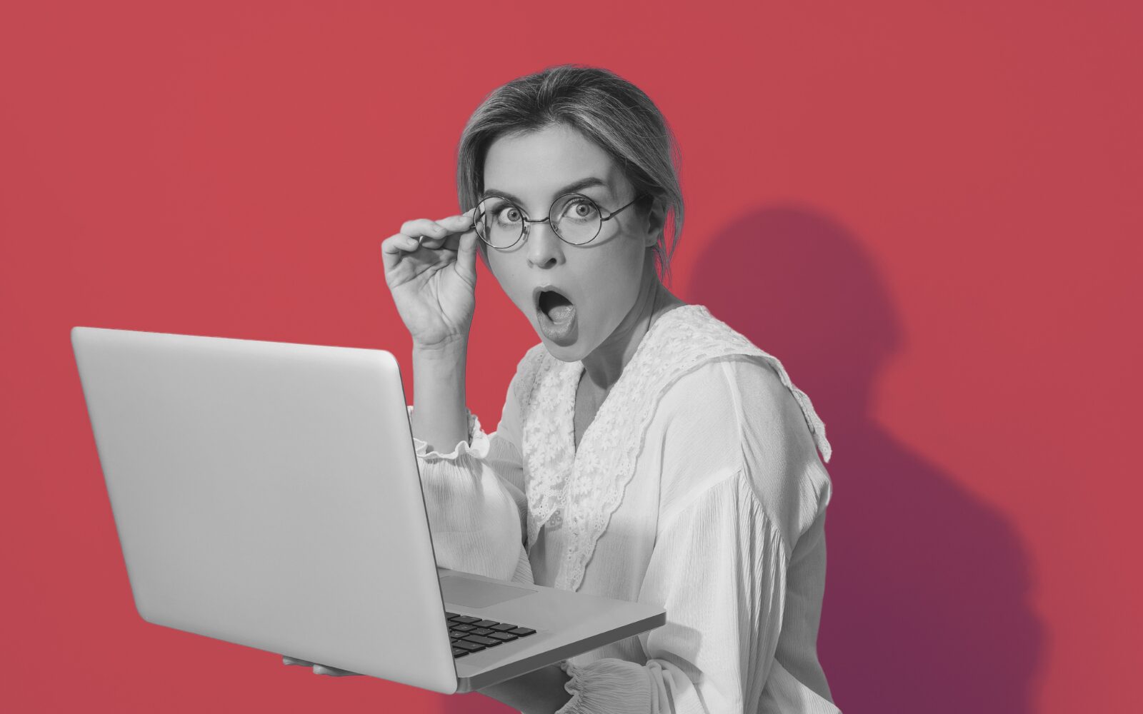 Woman looking at the camera with a shocked expression while holding a laptop